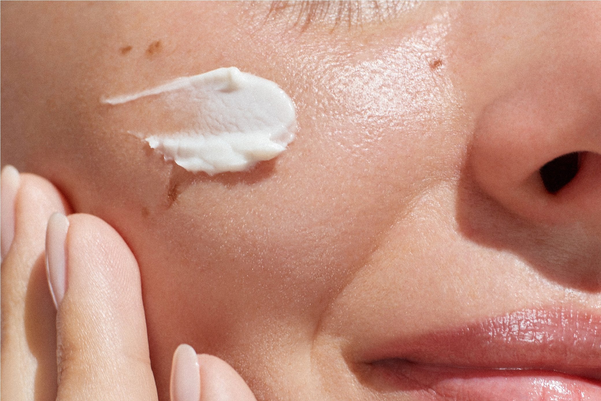 Up close image of a girl applying a cream to her face.