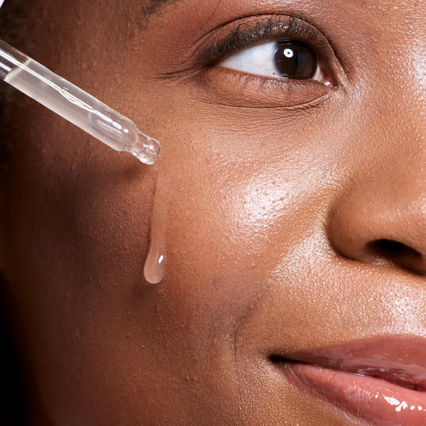Close-up of a woman applying a dropper of skincare product to her face.