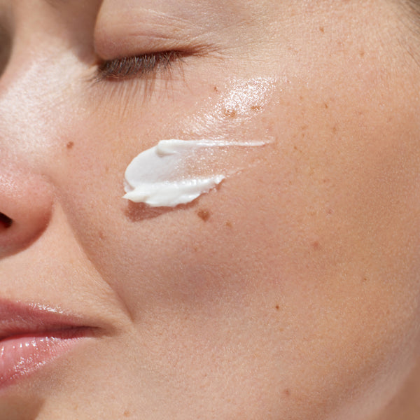 Close-up of a woman's face with a small amount of white cream on her cheek.