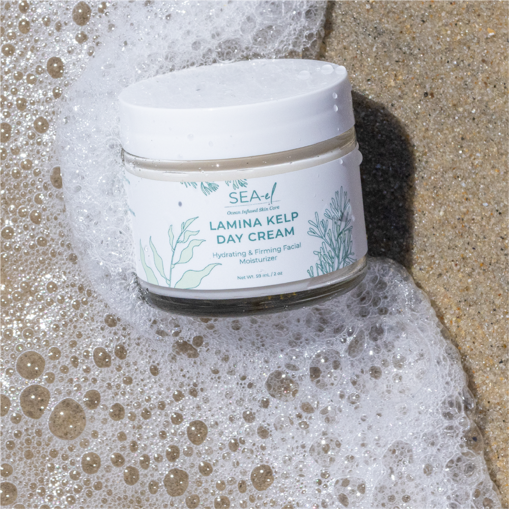 Picture of our Lamina Kelp Day Cream in the ocean water, on the sand.