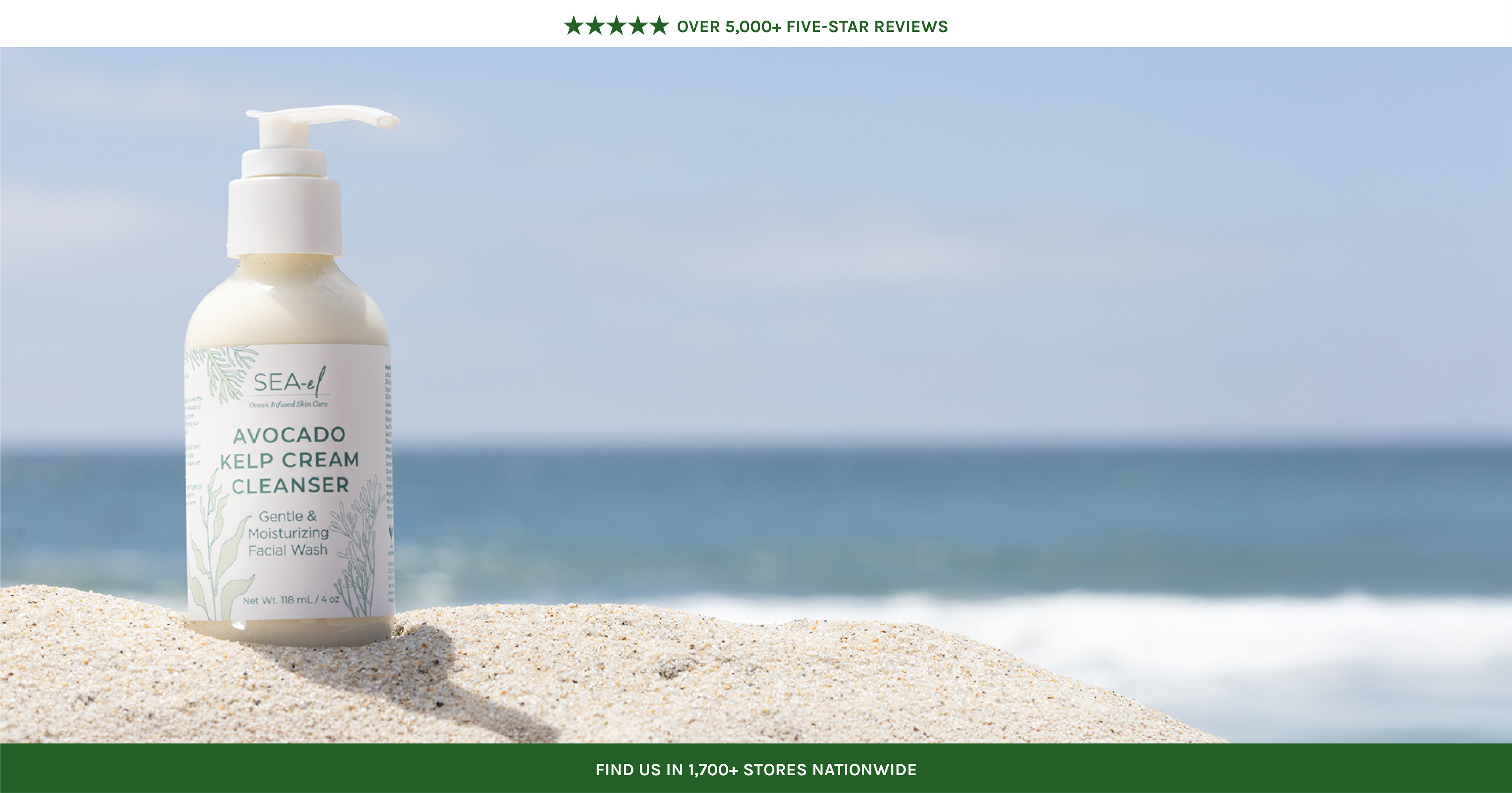 Skincare bottle labeled 'Avocado Kelp Cream Cleanser' on a beach with ocean in the background
