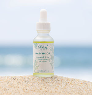 Our Matcha Oil dropper set on the sand by the ocean.