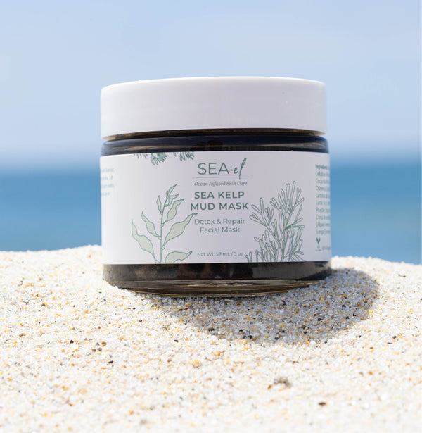 Sea Kelp Mud Mask sitting on the beach, in the sand, with the ocean horizon on the backround.
