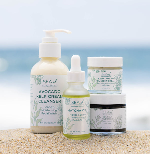A collection of skincare products including a facial cleanser, Facial oil dropper, and two jars, one for skin care masks, and one for hydration all labeled with 'SEA EL SKINCARE.' All sitting on the beach with the ocean in the backround.