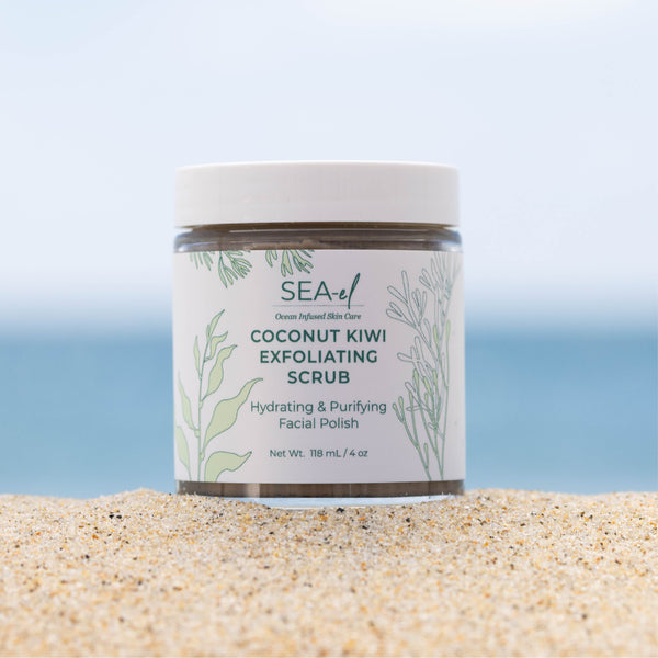 Picture of our Coconut Kiwi Exfoliating Scrub on the sand, at the beach with the ocean in the backround.