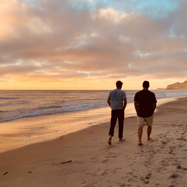 Two people walking on the beach during sunset.
