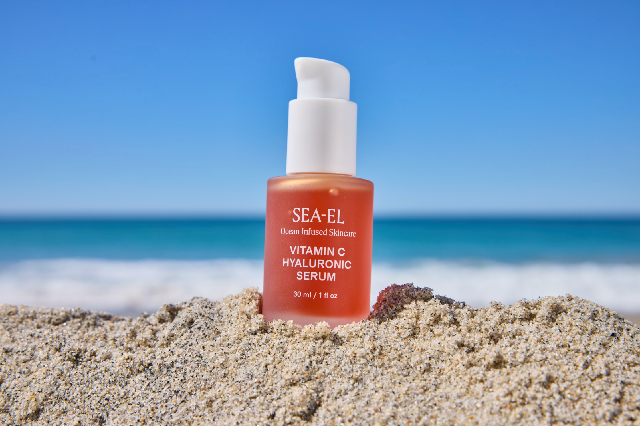 Our Vitamin C Hyaluronic Serum sitting in the sand at the beach.
