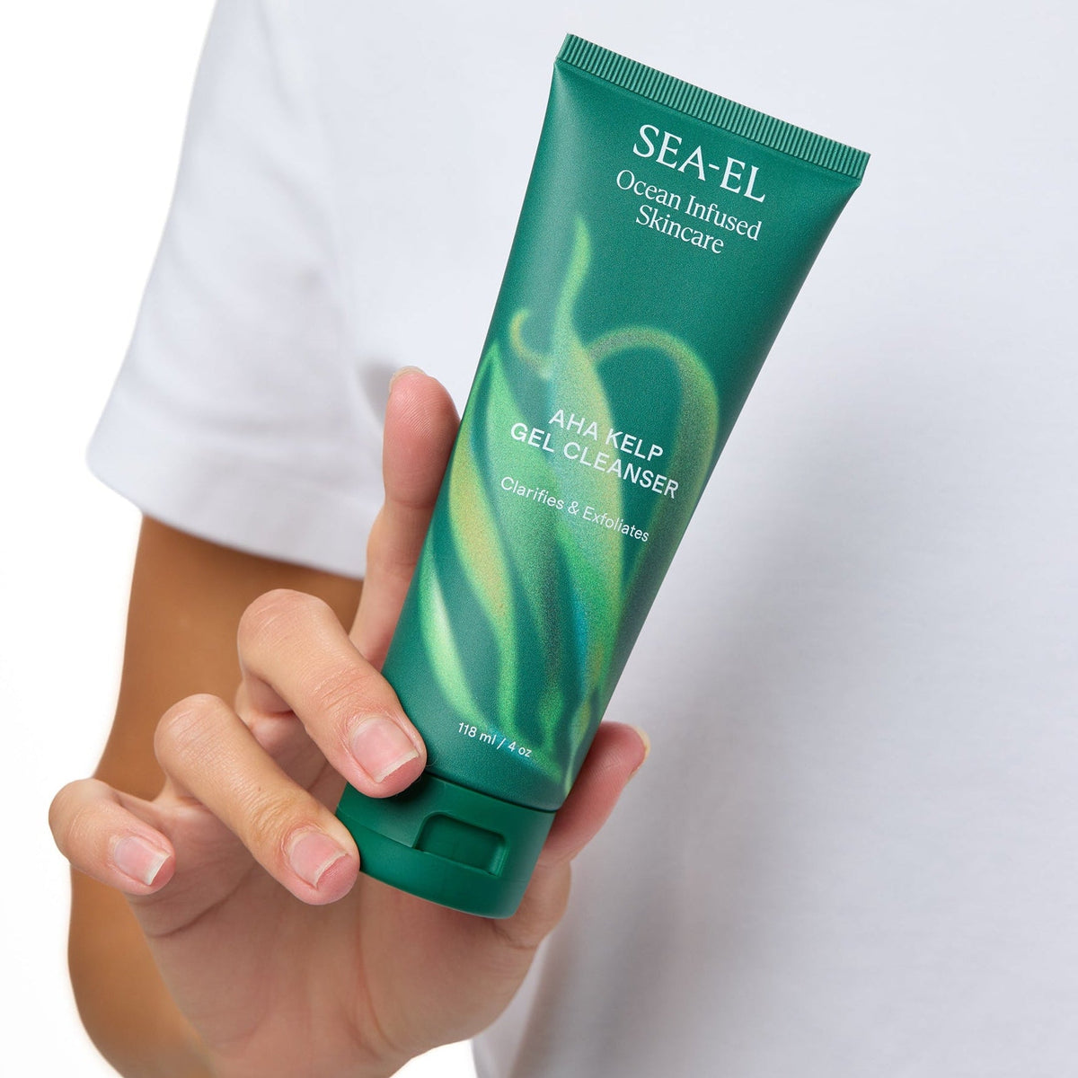 A person in a white t-shirt holds a green tube of SEA-EL Advanced Hair Regrowth Shampoo against a white background.