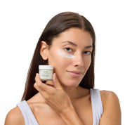 A woman with a white face mask on her cheek holds a small jar of NAELE Hyaluve White Peeling Mask against a clean white background.
