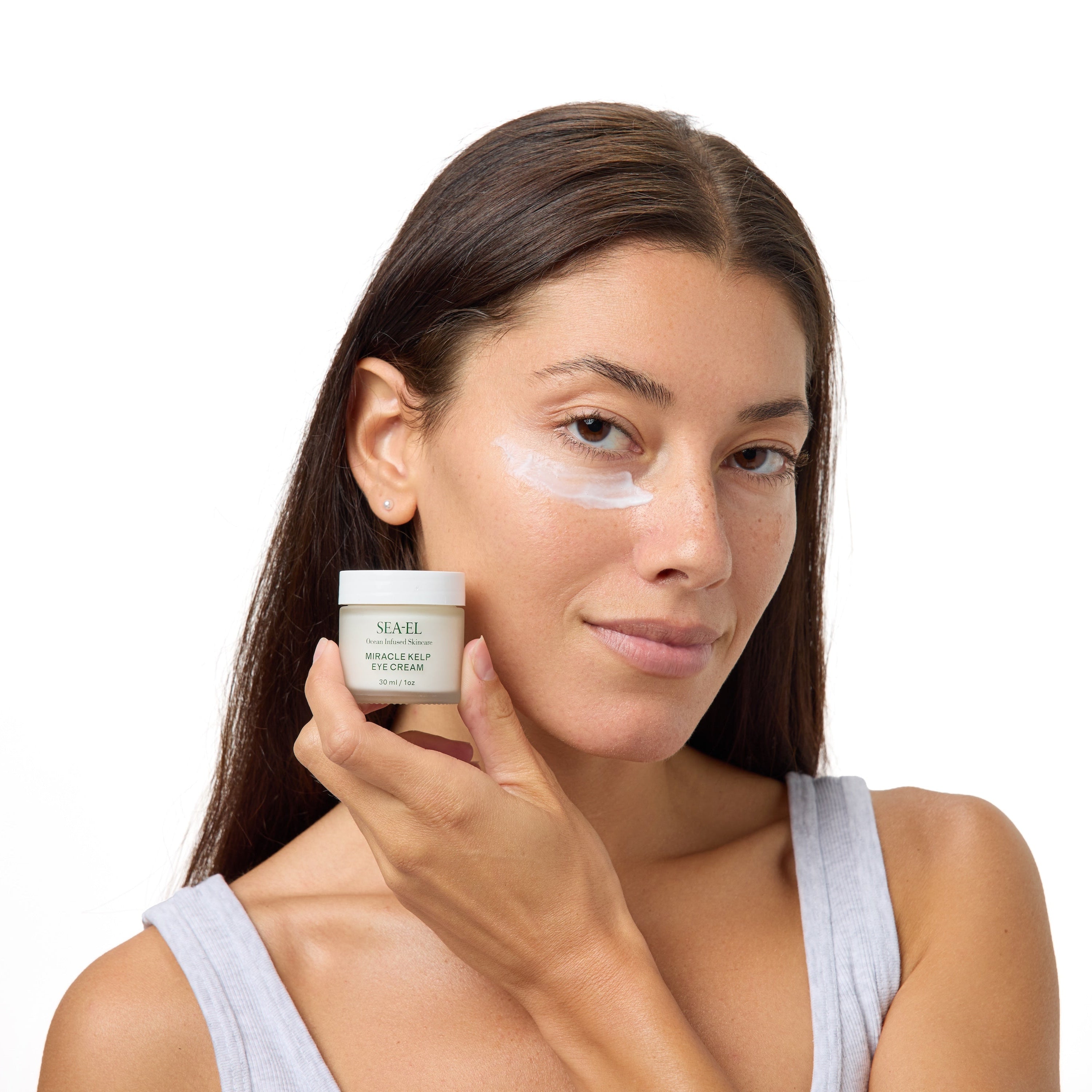 A woman with a white face mask on her cheek holds a small jar of NAELE Hyaluve White Peeling Mask against a clean white background.