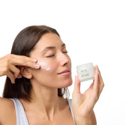 Women holding the Lamina Kelp Day Cream jar, while applying it to her cheek.