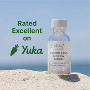 Bottle of Sea-El Castor Lash & Brow Serum on sand with a blue sky background. 